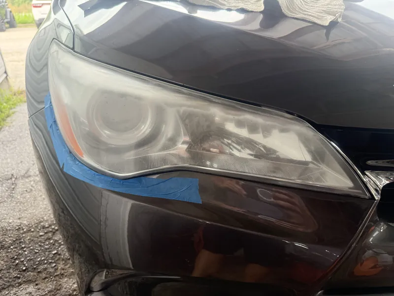 Cloudy, yellowed headlight lens on a gray Toyota Camry, masked off ready for restoration